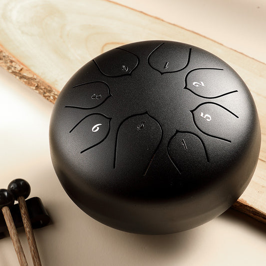 A steel tongue drum with a round, smooth surface, featuring multiple tones and accompanied by drumsticks and finger cots.