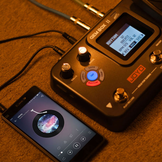 A pedal drum electromechanical guitar with a digital effect device, connected to a smartphone, displaying an app for the guitar.
