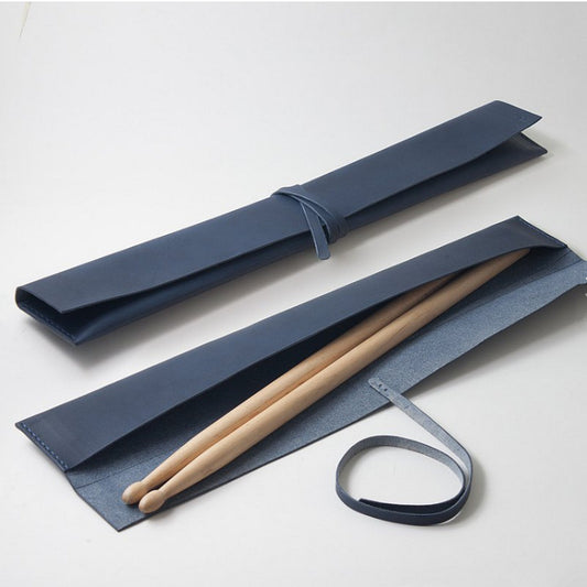 A navy blue drumstick bag unfolded on a white surface with a pair of drumsticks partially inserted into it, tied with a blue ribbon.