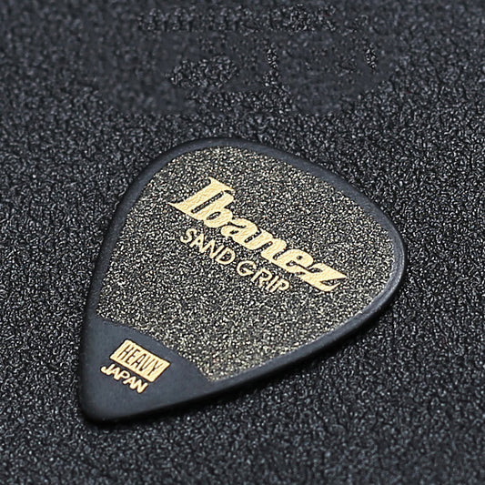 A close-up image of a black Ibanez sand grip guitar pick with a textured surface and the brand name 'Ibanez' printed in gold lettering.