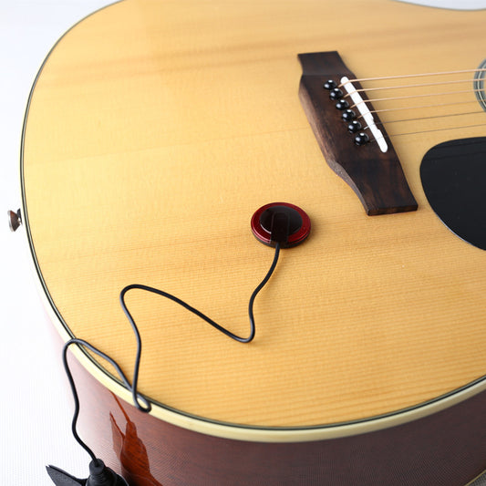 A piezoelectric element attached to the body of an acoustic guitar, connected by a cable to an amplifier.