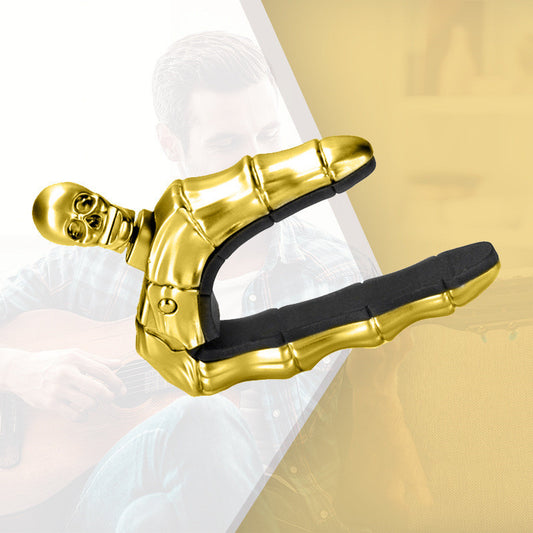 A gold-colored metal guitar capo with a skull design.