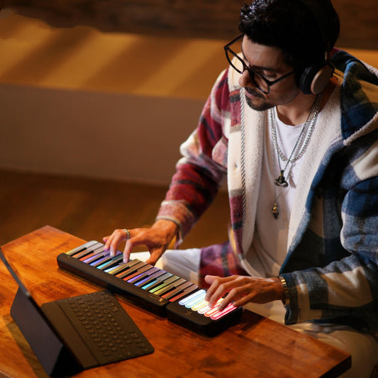 A person seated at a wooden table is playing a colorful, compact electronic piano that is angled towards them.