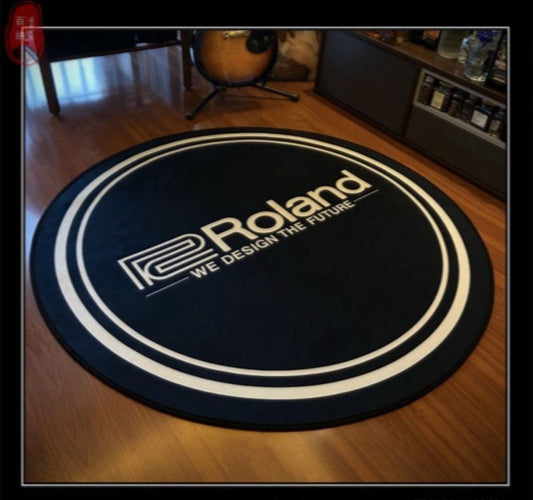 A round black carpet with the Roland logo in white, placed on a wooden floor, presumably serving as a sound insulation pad for a drum set.