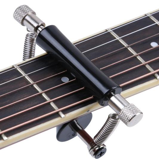 A black guitar sliding capo placed on the fretboard of an acoustic guitar.