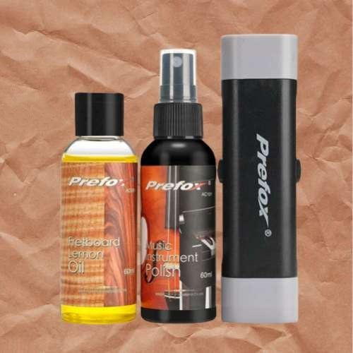 A collection of guitar care products including a bottle of lemon oil, a spray bottle of instrument polish, and a black cloth, all branded by Prefox.