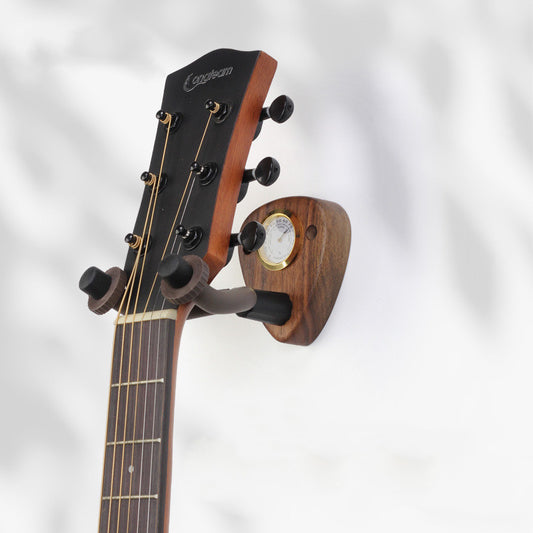 A wooden guitar hook mounted on a wall, with a moisture meter, holding a guitar.