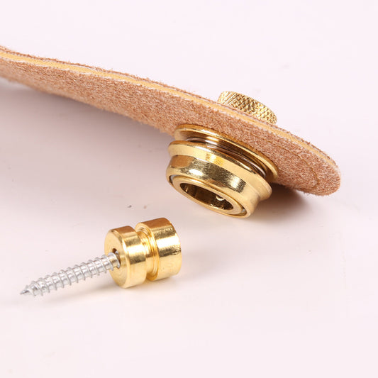 Gold-colored strap lock for a guitar or similar instrument, consisting of a buckle and a screw-like adjustment mechanism, placed on a light-colored surface.