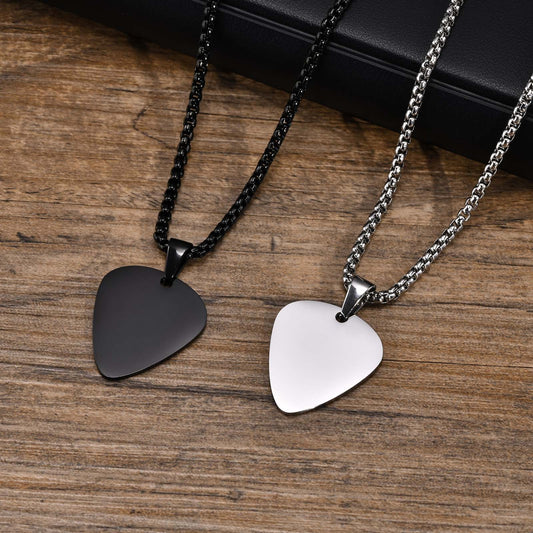 Two guitar pick pendants, one black and one silver, attached to chains laid out on a wooden surface.