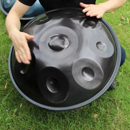 A person playing a carbon steel hand drum instrument laid on the grass.