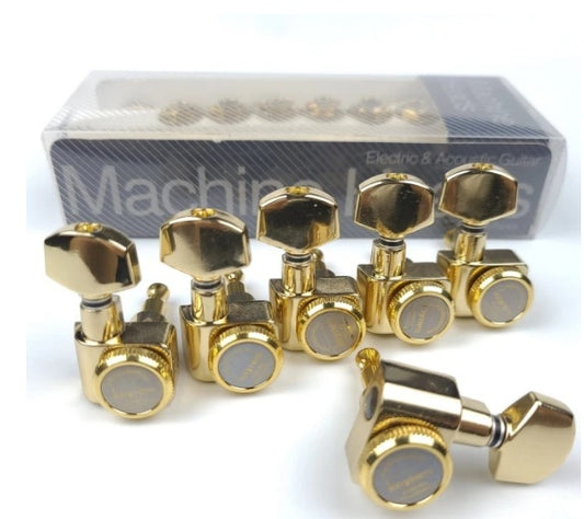 A set of gold-colored guitar tuning pegs with black and white details, displayed in front of a transparent package with the brand 'Machete' visible.