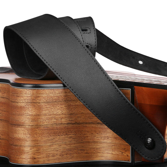 A black leather guitar strap laid over the body of an acoustic guitar.
